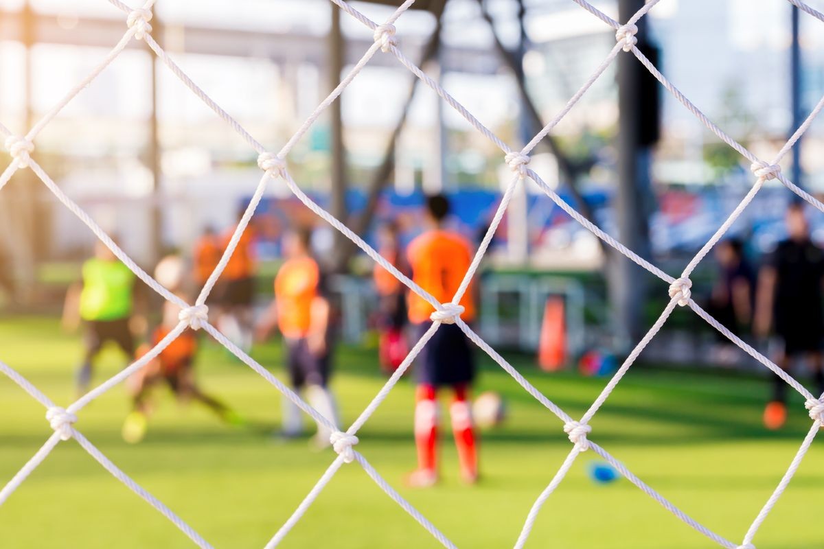 White mesh of goal with blurry soccer players. Soccer academy.